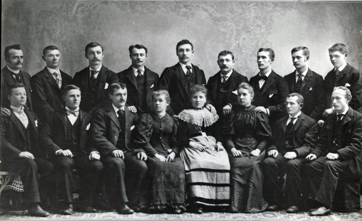 Gruppenfoto mit Einzelauswanderern aus dem Bezirk Leuk in den Vereinigten Staaten (Chicago). Die hier abgebildeten jungen Leute arbeiteten bei ihrem als temporär geplanten Aufenthalt im Gastgewerbe. Die Reise wurde vermutlich von Vinanz Oggier organisiert. Hintere Reihe die letzten 3 Personen rechts: die Brüder Vinanz und Alfred Oggier; ganz rechts Alex Oggier (späterer Schwager). Die Frau im hellen Kleid stammt aus Siders, rechts und links von ihr sitzen die beiden Schwestern Luise und Isabelle Kreuzer. Von den abgebildeten Personen stammen acht aus Turtmann (auch die Kreuzer-Schwestern), die übrigen vermutlich aus Unterbäch, Eischoll und Ergisch. Sechs von ihnen kehrten später ins Wallis zurück.